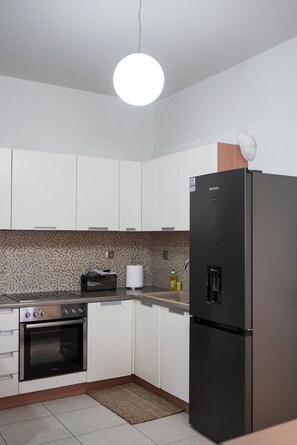 A modern kitchen with white cabinets, a stainless steel oven, a black refrigerator, and a round ceiling light. - Syros Sun Airport Villa Open Views Near Ermoupoli (Syros)