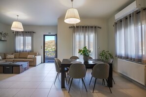 A spacious living area with a sofa, dining table, chairs, pendant lights, and a view through a door. - Syros Sun Airport Villa Open Views Near Ermoupoli (Syros)