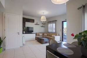 A modern living room with a sofa, coffee table, TV, and dining area with a table and chairs. - Syros Sun Airport Villa Open Views Near Ermoupoli (Syros)