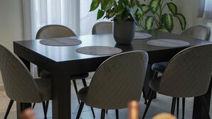 Ein Essbereich mit Tisch, Stühlen, einer Topfpflanze und einem Korb voller Gegenstände auf dem Tisch.