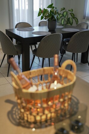 A dining area with a table and chairs, a potted plant, and a basket of items on the table. - Syros Sun Airport Villa Open Views Near Ermoupoli (Syros)