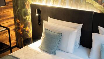 A neatly made bed with white linens and multiple pillows, a headboard with a light fixture, and a wall with a tropical mural.