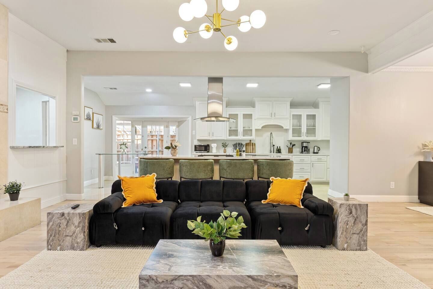 A modern living room with a sectional sofa, a marble coffee table, and a kitchen in the background.