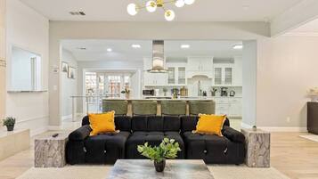 A modern living room with a sectional sofa, a marble coffee table, and a kitchen in the background.