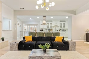Una sala moderna con un sofá modular, una mesa de centro de mármol y una cocina al fondo.