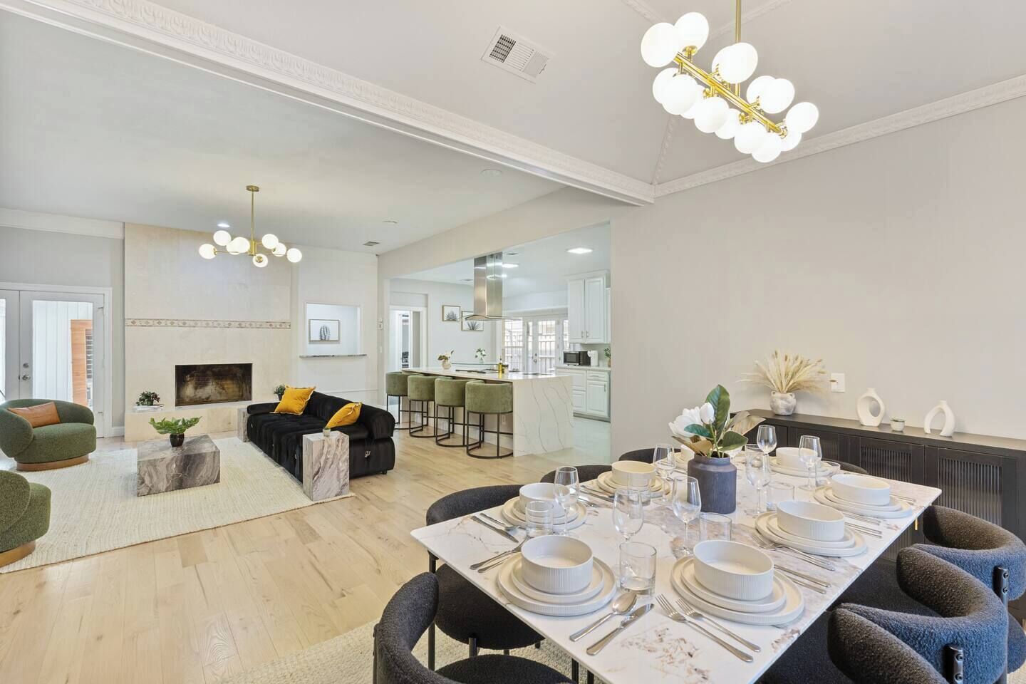 A modern living room with a sofa, a dining table set for four, and a kitchen in the background.