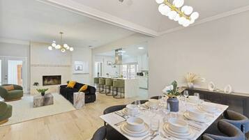 A modern living room with a sofa, a dining table set for four, and a kitchen in the background.