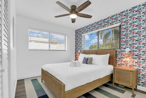A bedroom with a bed, a ceiling fan, a window with blinds, and a wall with a patterned wallpaper. - Stylish Surf-Themed Beach House with Private Pool Near Pompano Beach Pier, Pompano Beach Florida (Pompano Beach)