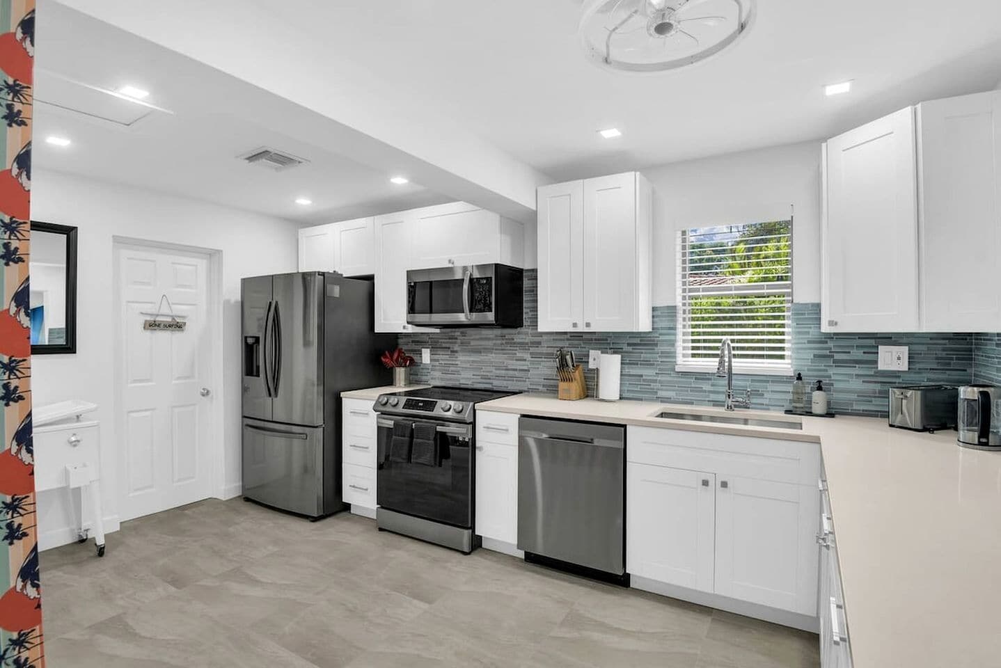 A modern kitchen with stainless steel appliances, white cabinetry, and a tiled backsplash.
