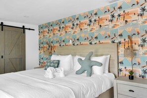 Ein Hotelzimmer mit einem Bett, einem Holzkopfteil, einem Nachttisch und einem Wandbild mit Strandmotiv.