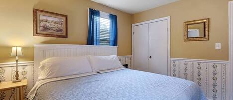 A bedroom with a bed, a nightstand, a lamp, a door, and a framed picture on the wall.