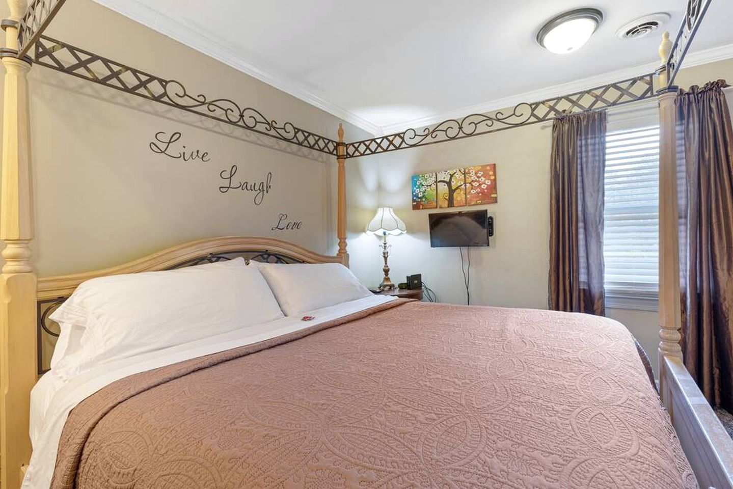 A bedroom with a bed, a wall with 'Live Laugh Love' text, a TV, and curtains.