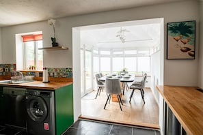 Una cocina moderna con lavadora, un comedor con mesa y sillas, y un ventanal que proporciona luz natural.