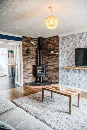 A living room with a fireplace, a TV mounted on the wall, and a wooden coffee table. - The Artisan House | Stylish Bedfordshire Escape (Stewartby)