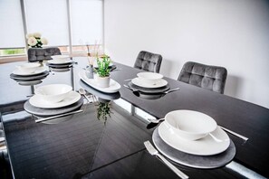A dining table set with white plates, bowls, and cutlery, with a potted plant centerpiece. - The Artisan House | Stylish Bedfordshire Escape (Stewartby)
