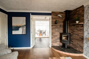 Una sala de estar con chimenea, un comedor con sillas y una mesa, y una pared azul con un cuadro enmarcado.