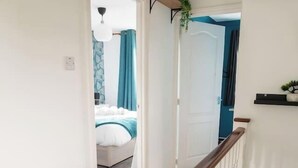 Ein Flur mit Holzbalken, weißen Wänden und einer Tür zu einem Schlafzimmer mit Bett und blauen Vorhängen.