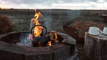A campfire with a kettle and mugs, surrounded by rocks and a wooden stump.