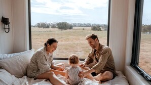 A family of three on a bed with a view of a grassy field through a window. - Magical Tiny House with Amazing Stargazing and Deck in Victoria (Skipton)