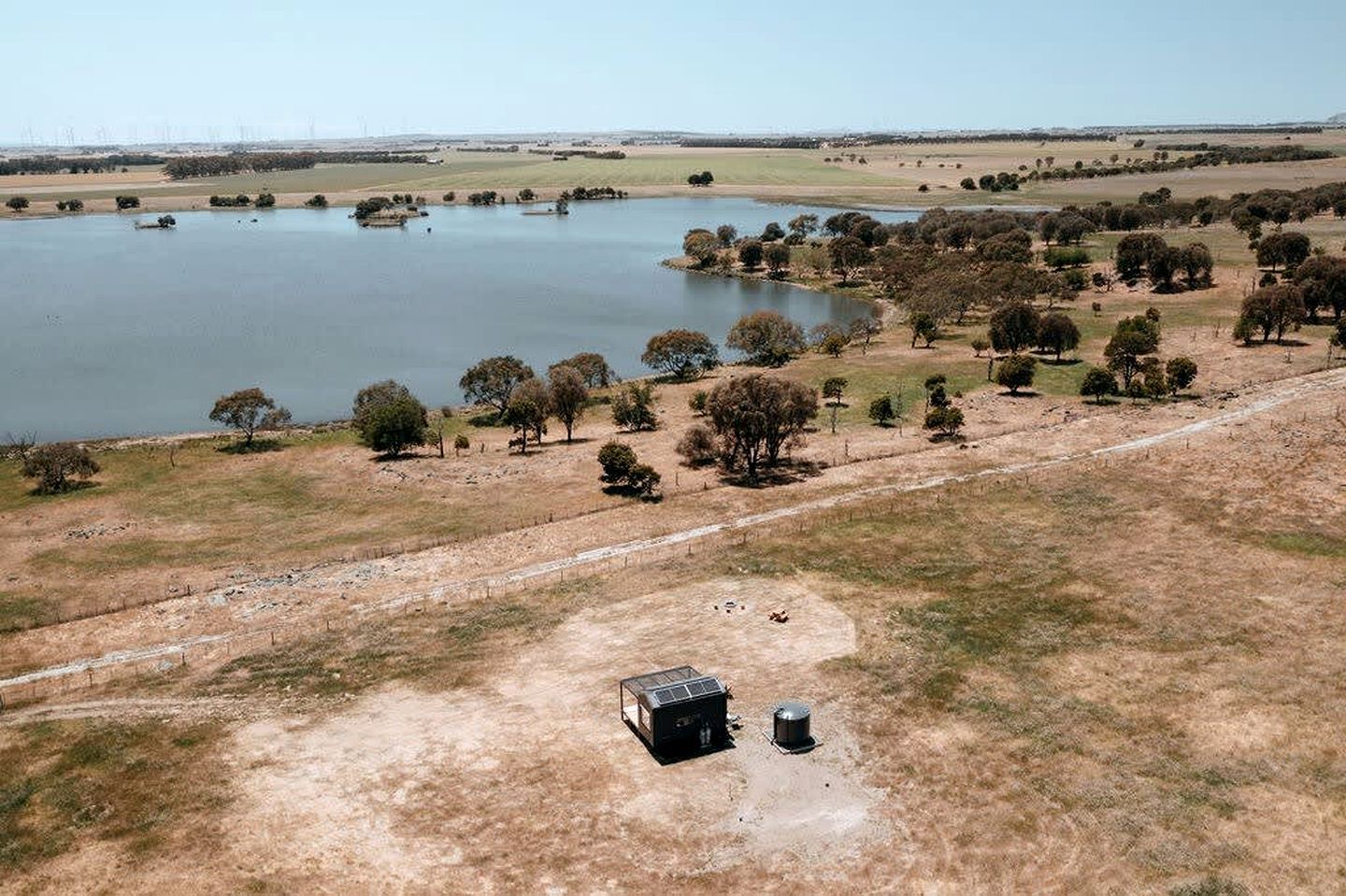 An aerial view of a rural landscape with a lake, trees, and a fenced area with a small building.