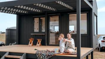A modern, dark-colored cabin with a wooden deck, a small table, and a bench.