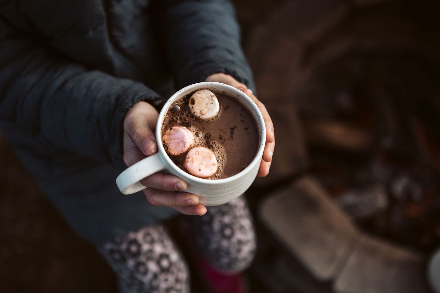 A person holding a mug with a hot beverage and marshmallows.