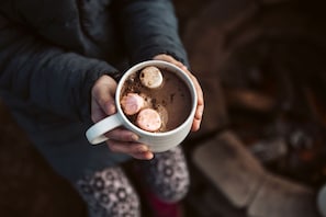 A person holding a mug with a hot beverage and marshmallows.