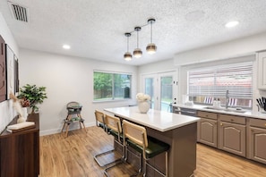 A modern kitchen with a central island, wooden flooring, and pendant lighting.