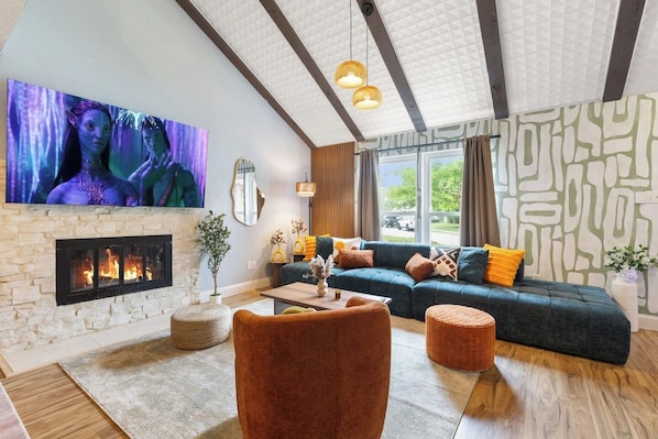 A modern living room with a fireplace, a large flat-screen TV, a sofa with cushions, and a coffee table.