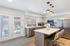 A modern kitchen with a central island, stainless steel appliances, and a sliding glass door leading to an outdoor seating area.