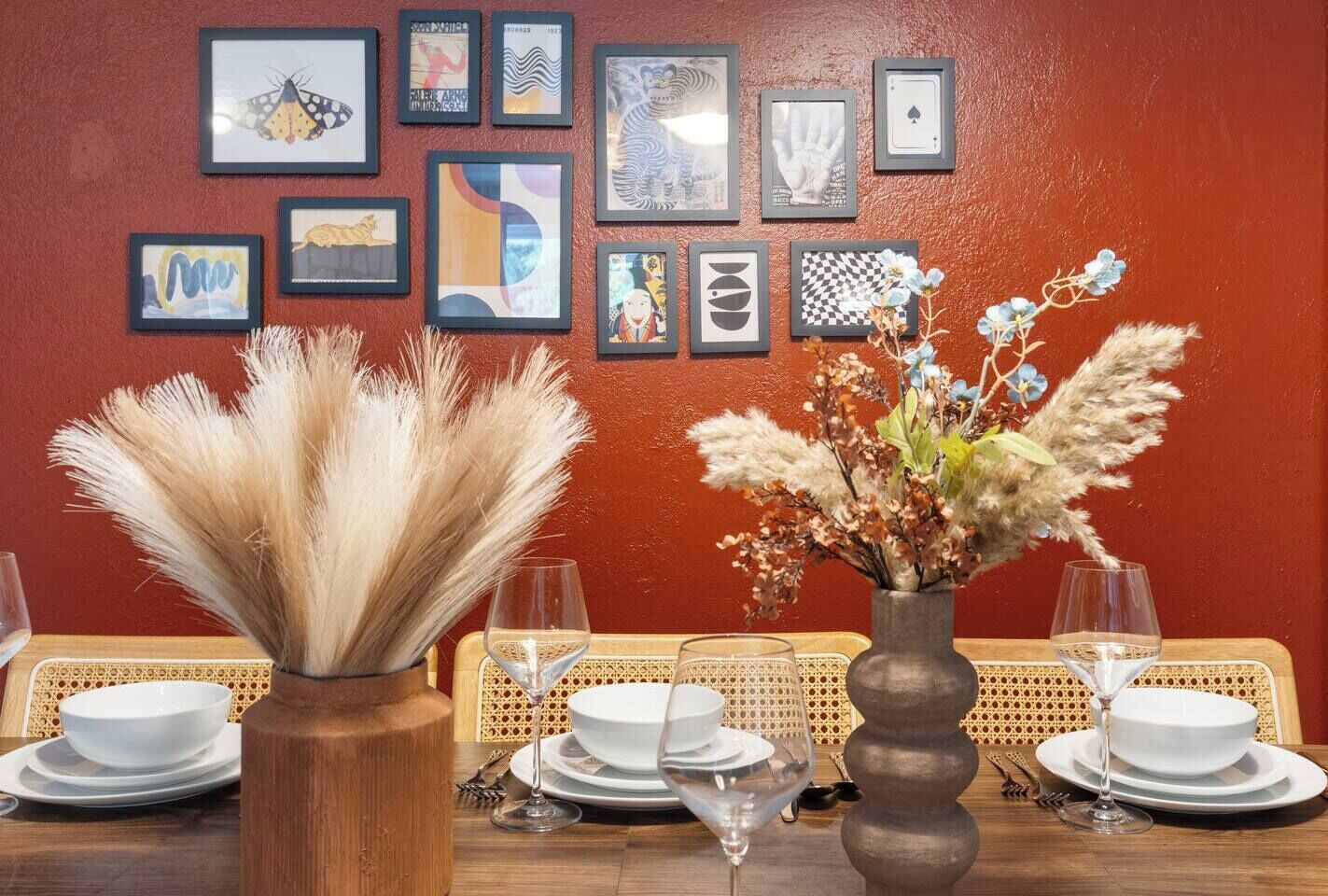 Une table à manger dressée avec des assiettes, des verres et un vase contenant des fleurs séchées.