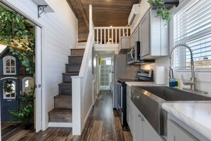 A kitchen with a stainless steel sink, a microwave, and a stove. There is a wooden staircase leading to a second floor. - Enchanting Hill Country Vacation Home with Storybook Loft Near Fredericksburg, TX (Fredericksburg)