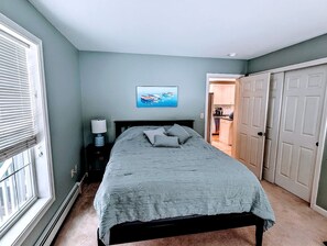 A bedroom with a bed, a nightstand, a wall-mounted lamp, a painting, and a closet. - Spacious Family Vacation Home with Fire Pit Near Acadia National Park | Bar Harbor, Maine (Bar Harbor)