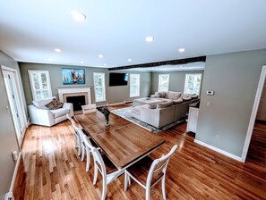 A modern living room with a wooden dining table, white chairs, a sofa set, and a fireplace. - Spacious Family Vacation Home with Fire Pit Near Acadia National Park | Bar Harbor, Maine (Bar Harbor)
