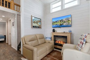 Ein gemütliches Wohnzimmer mit einem beigen Sofa, einem Kamin, einem darüber montierten Fernseher und einem Gemälde an der Wand.