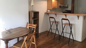 Een eethoek met een houten tafel en stoelen, een keuken met houten kasten, en hanglampen.