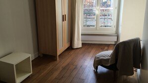 Een kamer met een houten garderobe, een raam met uitzicht op gebouwen en een stoel.