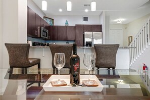 A modern kitchen with dark cabinets, a microwave, and a refrigerator. There is a dining table with two chairs and a bottle of wine. - Modern Gated Townhouse with Heated Pool Access Near Beaches – Pompano Beach, Florida (Pompano Beach)