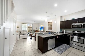 A modern kitchen with a central island, stainless steel appliances, and a dining area with a sofa and chairs. - Modern Gated Townhouse with Heated Pool Access Near Beaches – Pompano Beach, Florida (Pompano Beach)