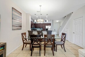 Un espace repas avec une table et des chaises, une cuisine à l’arrière-plan et un escalier menant à un autre niveau.