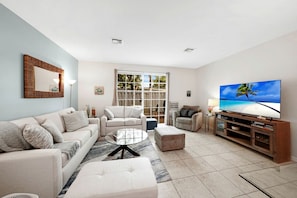 A living room with a sofa, armchairs, a coffee table, and a TV on a wooden stand. - Modern Gated Townhouse with Heated Pool Access Near Beaches – Pompano Beach, Florida (Pompano Beach)