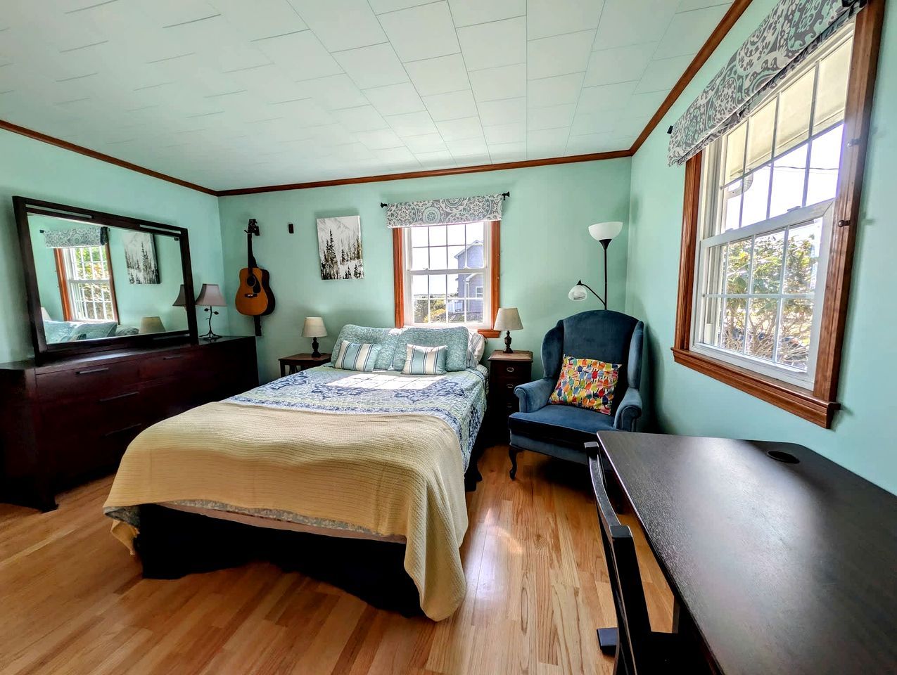 Een slaapkamer met een bed, een stoel, een bureau, een dressoir en een raam.