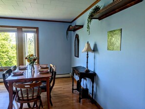 A dining area with a wooden table and chairs, a vase with flowers, and a lamp on a side table. - Scenic Coastal Cottage with Ocean Views Near Acadia National Park in Lamoine, Maine (Lamoine Point)