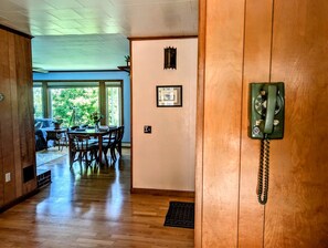 A wooden-floored hallway leading to a dining area with a table and chairs, a telephone on the wall, and a view of the outdoors. - Scenic Coastal Cottage with Ocean Views Near Acadia National Park in Lamoine, Maine (Lamoine Point)