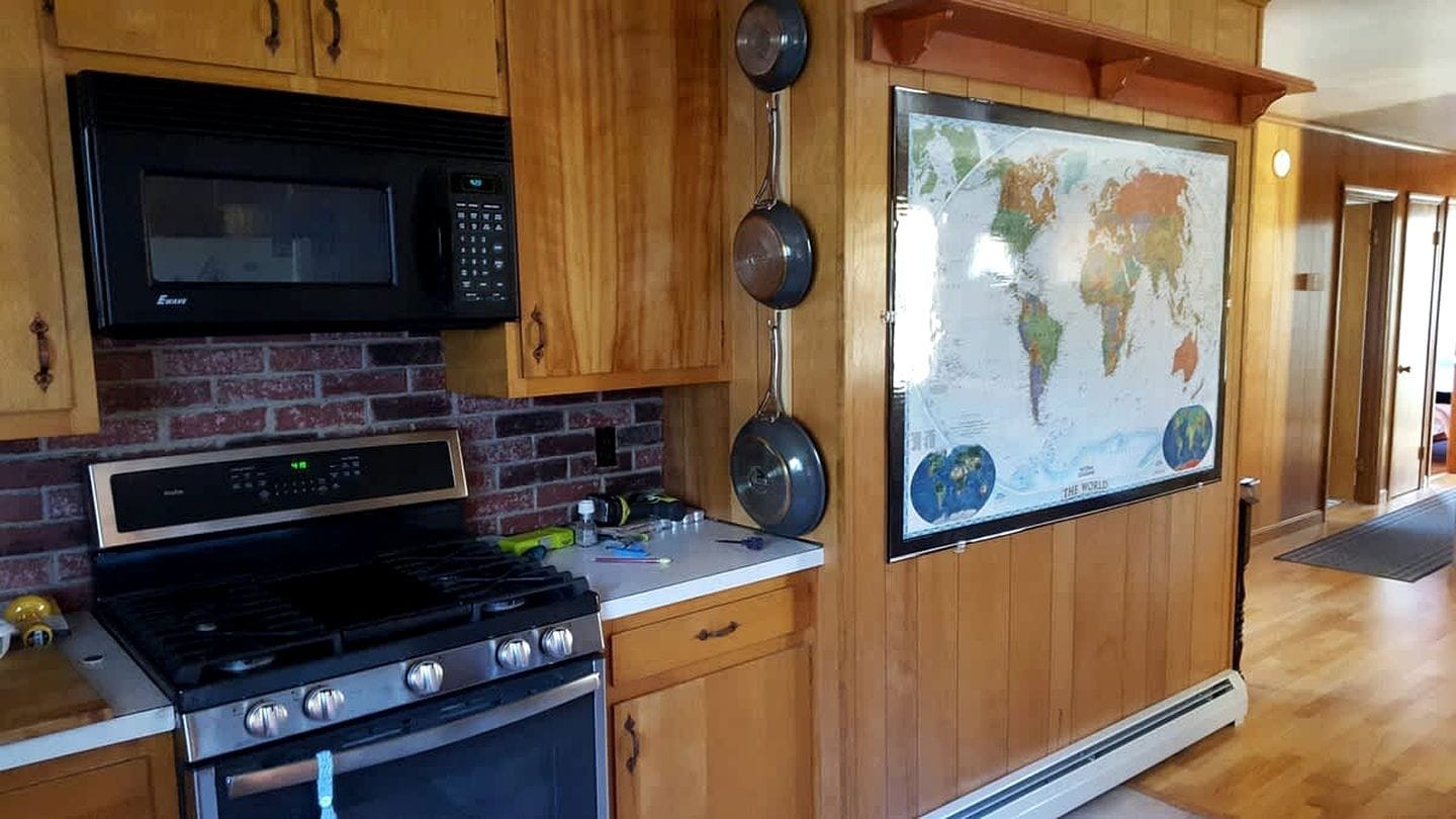 A kitchen with a stove, microwave, and a large world map on the wall.