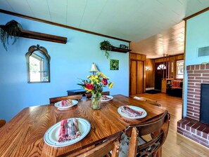 Une salle à manger avec une table en bois dressée pour six personnes, un vase de fleurs et une cheminée en briques.
