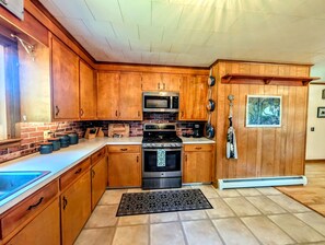 A kitchen with wooden cabinets, a stainless steel stove, a microwave, and a window with a view. - Scenic Coastal Cottage with Ocean Views Near Acadia National Park in Lamoine, Maine (Lamoine Point)