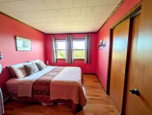 A bedroom with a bed, a wooden door, and a window with curtains. - Scenic Coastal Cottage with Ocean Views Near Acadia National Park in Lamoine, Maine (Lamoine Point)
