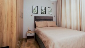 Un dormitori amb un llit, una tauleta de nit i tres quadres botànics al mur.