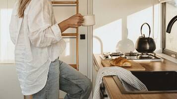 Una persona de pie en una cocina con una escalera de madera, una tetera y un croissant sobre la encimera.